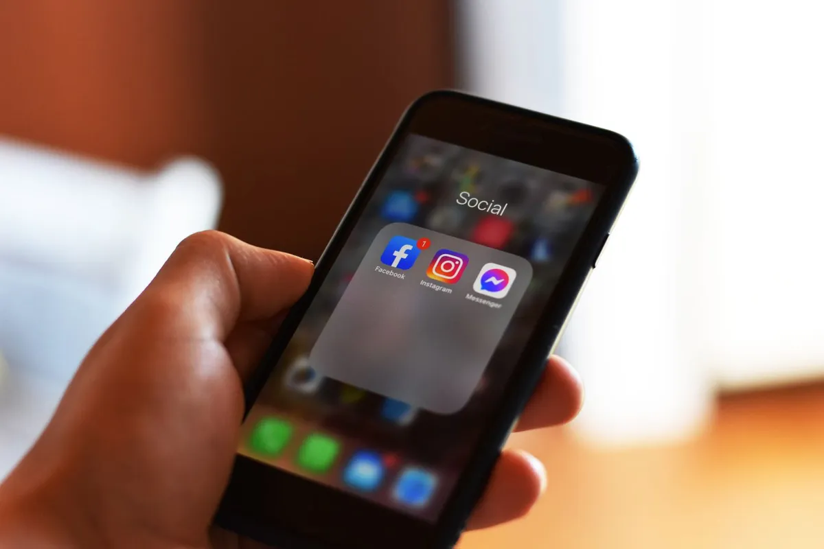 En hånd holder en mobil med sosiale medier-apper som Facebook og Instagram.