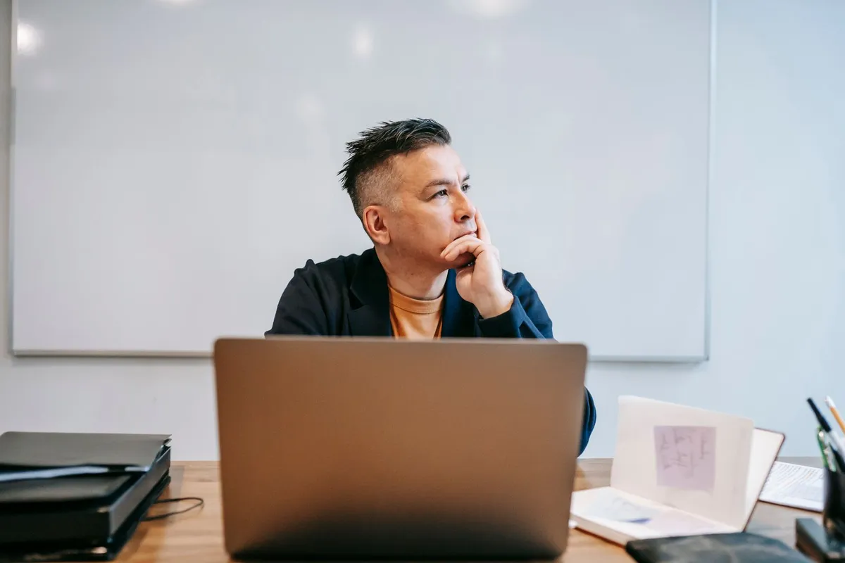 En person sitter ettertenksomt ved laptopen på et hjemmekontor.